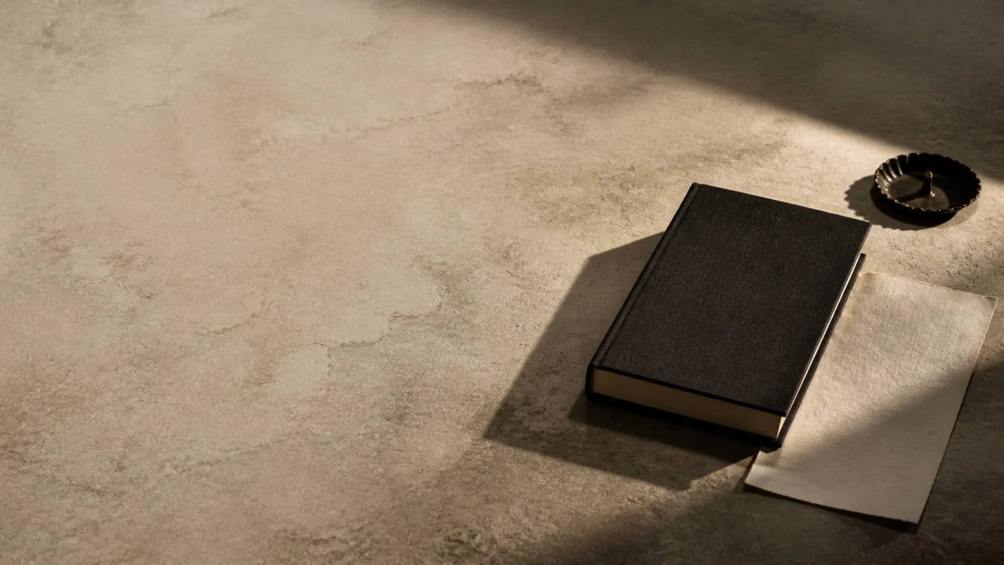 Mesa de pedra com um livro de capa dura fechado, sob luz lateral